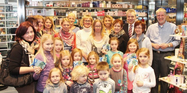 Zur Spendenübergabe durch Bürgermeister Gottfried Störmer waren Kinder und Betreuerinnen aus den sieben beteiligten Einrichtungen in die Parfümerie Heeß gekommen: Schülerbetreuung Hüttenfeld mit Ursel Senftner, KiTa Europaring mit Dorothea Roos und Lidia Wolf, KiTa Schwalbennest mit Melanie Wiesebrock, der Kindergarten Rosengarten mit Heike Jung, die Schillerschule mit Annette Wunder, KiTa Neuschloß mit Heike Heiß und die Schülerbetreuung Pestalozzischule mit Roswitha Rinkel. Die Geldpäckchen mit je 216 Euro waren hübsch verschnürt. Foto: Hannelore Nowacki