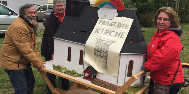 Pfarrer Martin Müller und die Mitglieder des Kirchenvorstandes Martina Wittmer und Monika Oswald „tragen“ symbolisch das Kirchenmodell, das auch am Infostand der Kirchengemeinde beim Maimarkt stehen wird, um für Spenden zur Finanzierung der Kircheninstandsetzung zu werben. Foto: oh