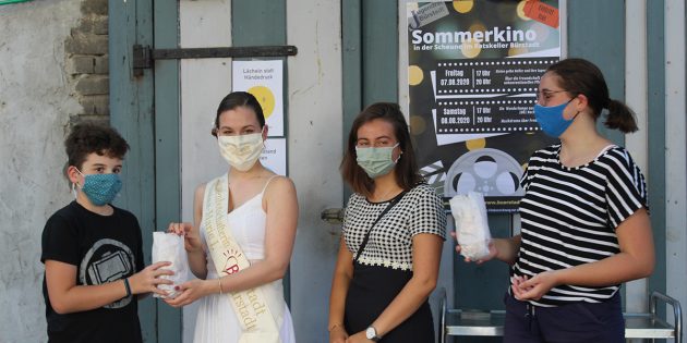 Kinobesucher Aron bekommt Popcorn von der Sonnenbotschafterin Luisa-Marie überreicht. Die tolle Idee für das Sommerkino stammt vom Jugendrat, hier durch Lilli Bardelang (rechts) und Anastasia Möller (2.v. rechts) vertreten. Foto: Eva Wiegand