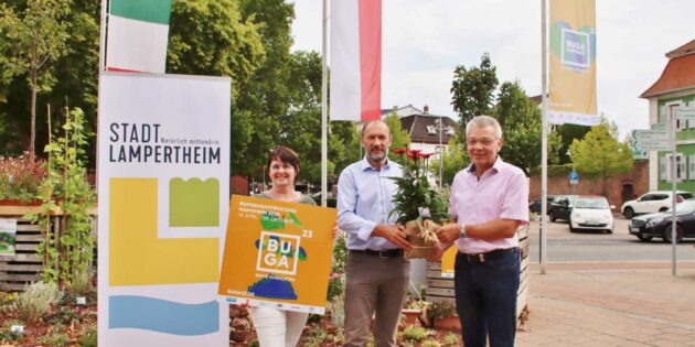 Der temporäre Garten auf dem Europaplatz hat mit dem blühenden Geschenk von BUGA-Geschäftsführer Michael Schnellbach (Mitte) für Bürgermeister Gottfried Störmer Zuwachs bekommen. Gemeinsam gehisst wurde die BUGA-Partnerfahne. Die Echinacea, ein roter Sonnenhut, sucht die Sonne, braucht aber auch Wasser zum Gedeihen, erklärte die Leiterin der Technischen Betriebsdienste Sabine Vilgis (links), die mit Dirk Dewald vom Stadtmarketing zur BUGA-Steuerungsgruppe gehört. Foto: Hannelore Nowacki