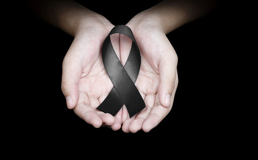 Hand holding black ribbon on black background mourning awareness sign