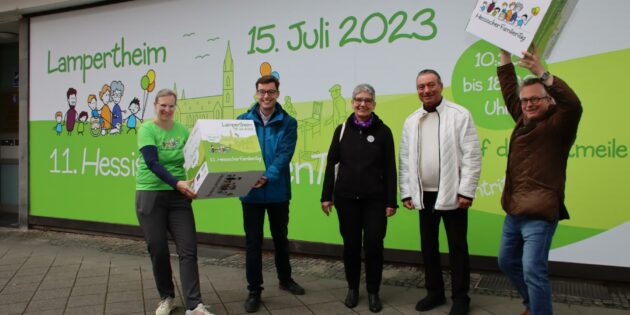 Das große Plakat an der Schaufensterfront in der Kaiserstraße 20 zwischen Stadt-Apotheke und Volksbank zeigt das offizielle Logo für den 11. Hessischen Familientag, das Dr. Ulrich Kuther von der Karl-Kübel-Stiftung (rechts) und Nadine Albers vom Hessischen Ministerium für Soziales und Integration (links) gemeinsam mit dem Ersten Stadtrat Marius Schmidt vorstellten. Pfarrerin Sabine Sauerwein informierte über das Gemeindefest der Lukasgemeinde und Kurt Oberfeld wies auf das Sommerfest hin. Foto: Hannelore Nowacki